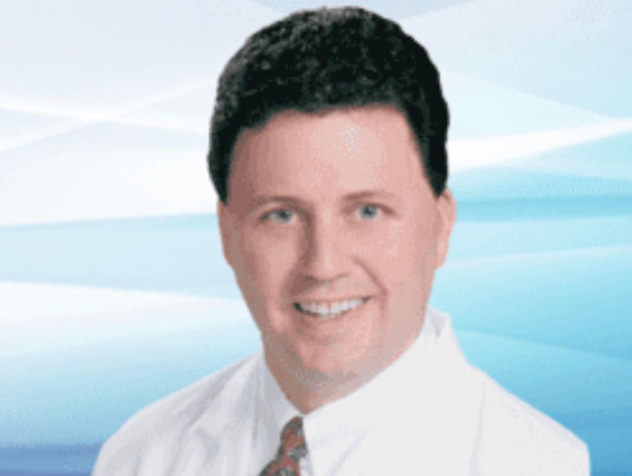 Doctor in a white coat smiles at the camera, against a light blue background.