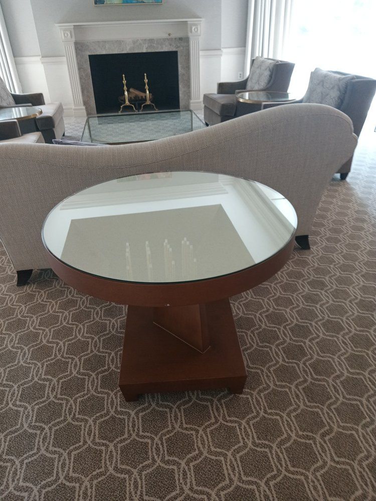 Round glass-topped table with a wooden base in a living room with a fireplace and seating.