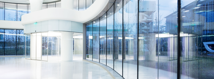 Modern, white building interior with curved glass windows reflecting a cloudy sky and exterior structures.