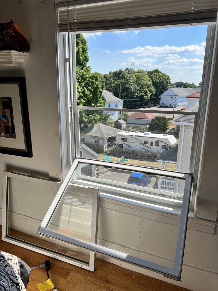 Open window, screen and frame lying on sill; view of houses and sky outside.