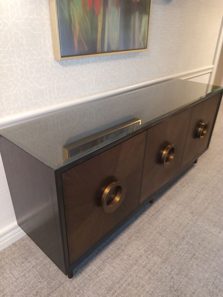 Dark wood cabinet with gold hardware, glass top, and abstract painting on wall.