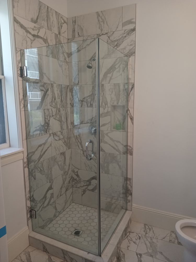 Marble-tiled shower with glass door and white walls; showerhead and shelving visible.
