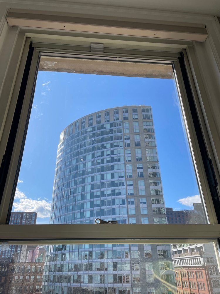 View of a curved, high-rise building through an open window against a blue sky.