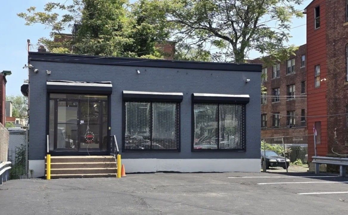 Dark gray building with three windows, roll-down shutters, and a wooden ramp.