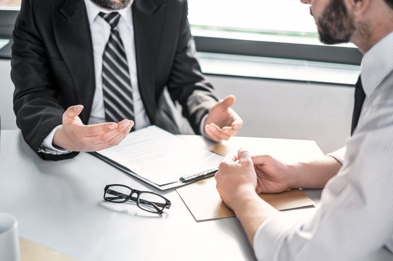 Two men are sitting at a table having a conversation over legal papers.