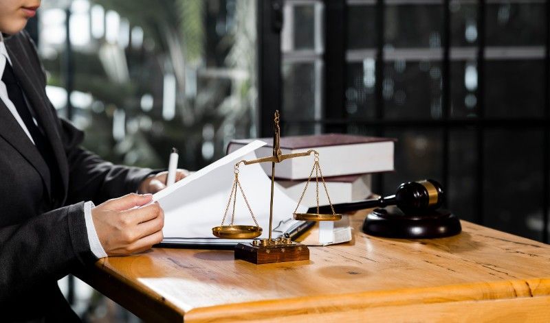 A lawyer is sitting at a wooden table with a gavel and scales of justice.
