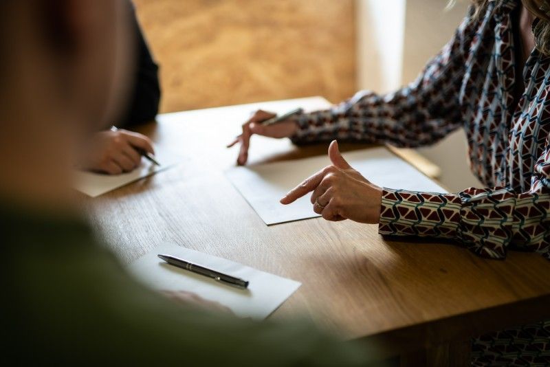A woman is pointing at a piece of paper while sitting at a table.