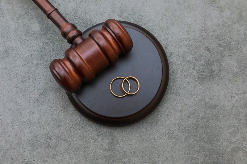 A wooden judge 's gavel with two wedding rings on it.