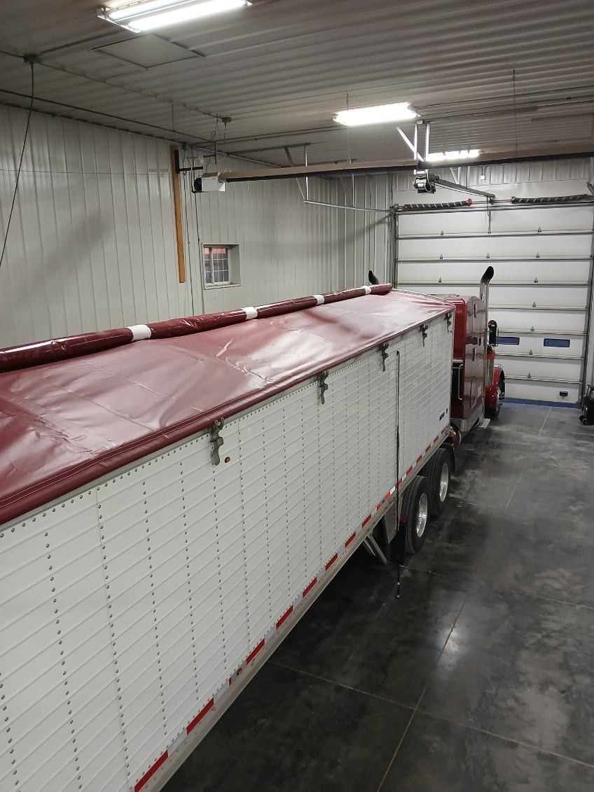 Semi-truck trailer inside a warehouse, unloading at a loading dock with a white corrugated side.