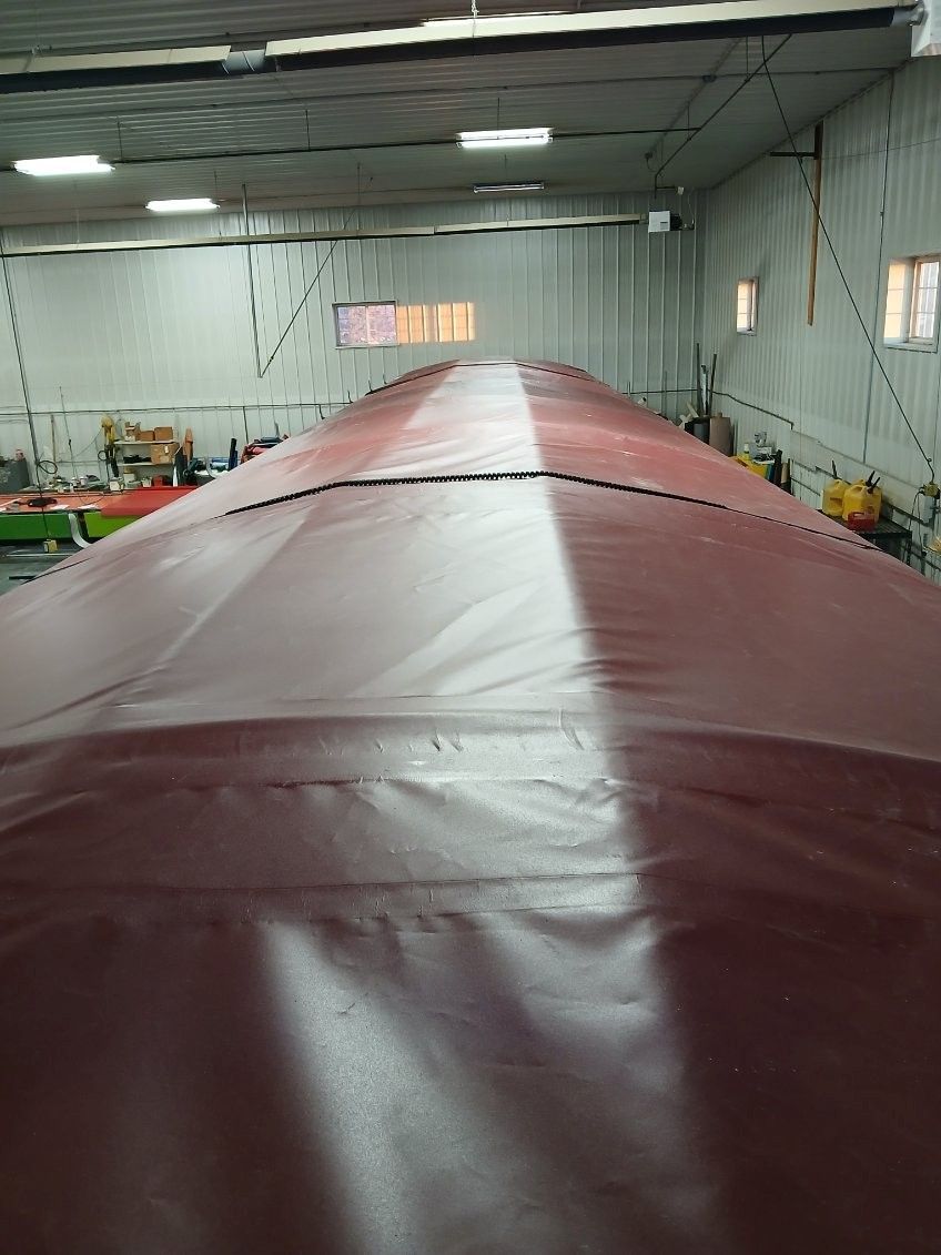 Red tarp covering a long, curved structure inside a large building.