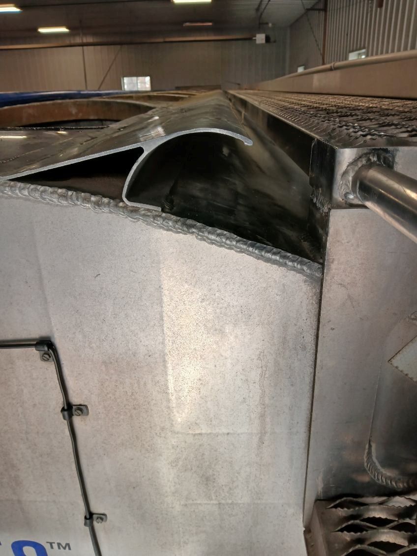 Aluminum structure with curved channel, riveted panels, and grating. Industrial setting.