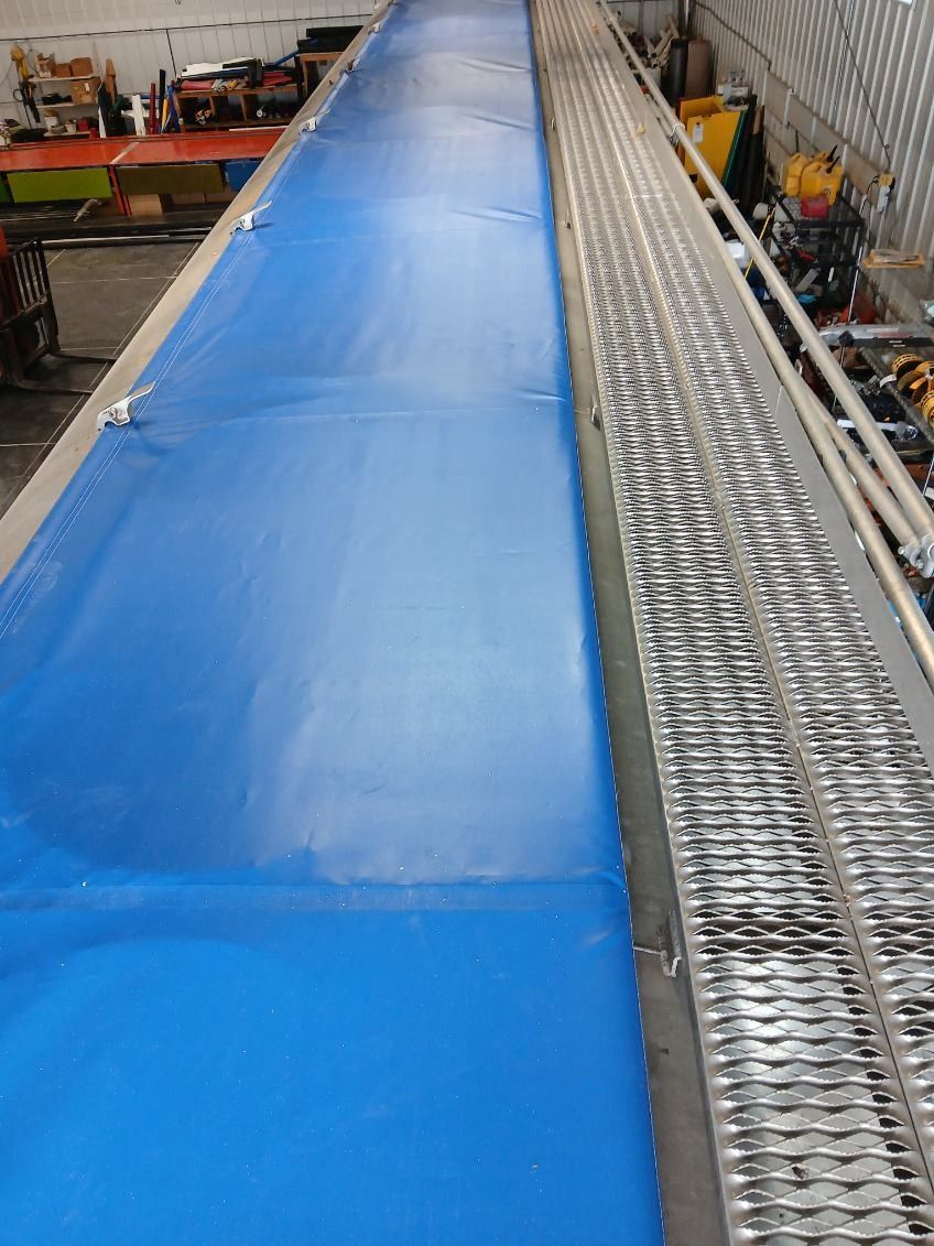 Blue tarp covering a long metal structure with a grated walkway on its side.