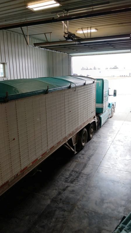 A semi-truck loaded with a covered cargo trailer, parked inside a warehouse loading dock.