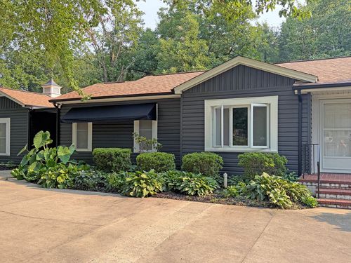 Single-story house with dark siding, white windows, red tile roof, and lush front landscaping