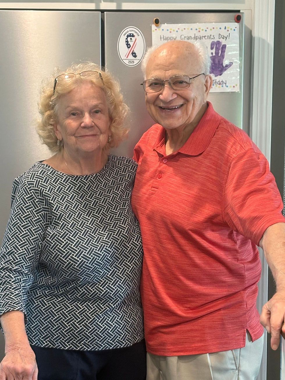 Smiling couple standing in a kitchen, with the man in a red shirt and the woman in a patterned top