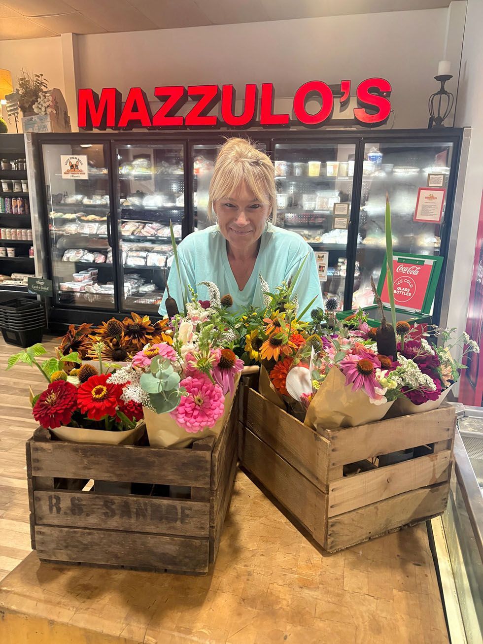 A woman smiling behind colorful flower arrangements in crates at Mazzulo’s Market counter