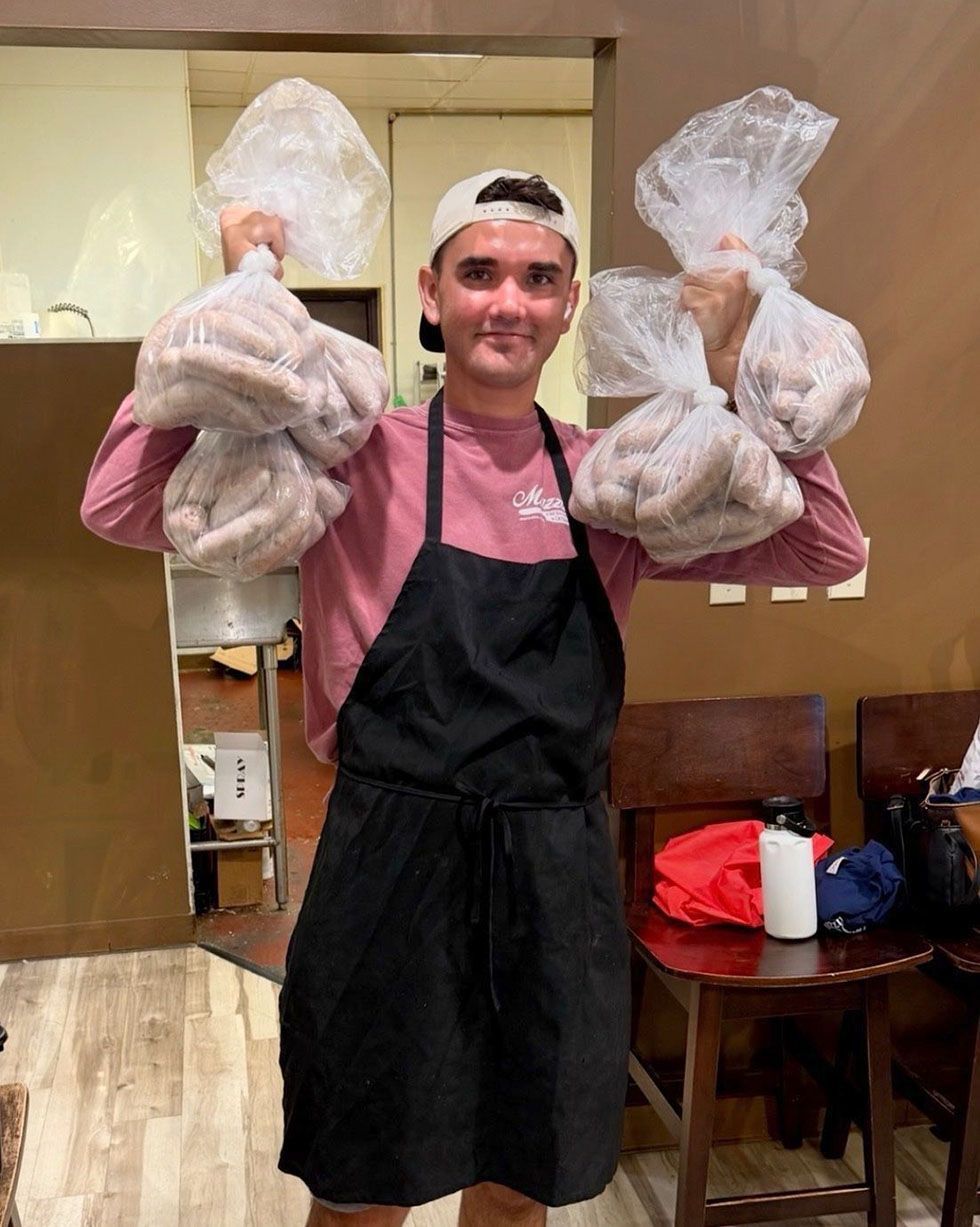 Person in a pink shirt and black apron holds two large bags of sausages