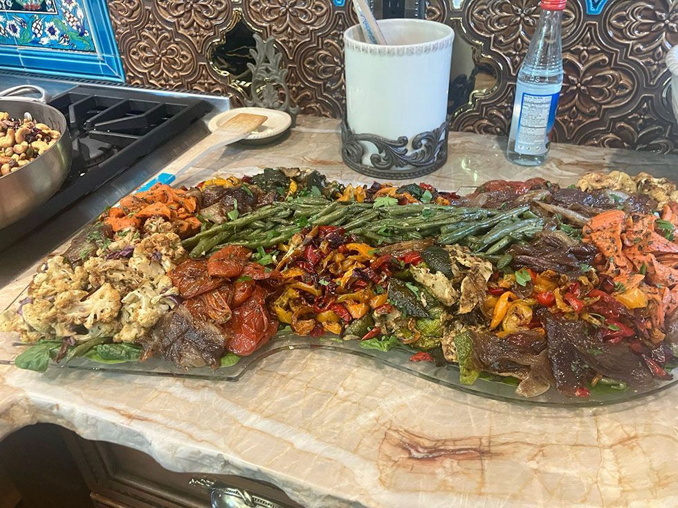 Large platter of grilled meat and vegetables on a table, with drinks and side dishes in the background