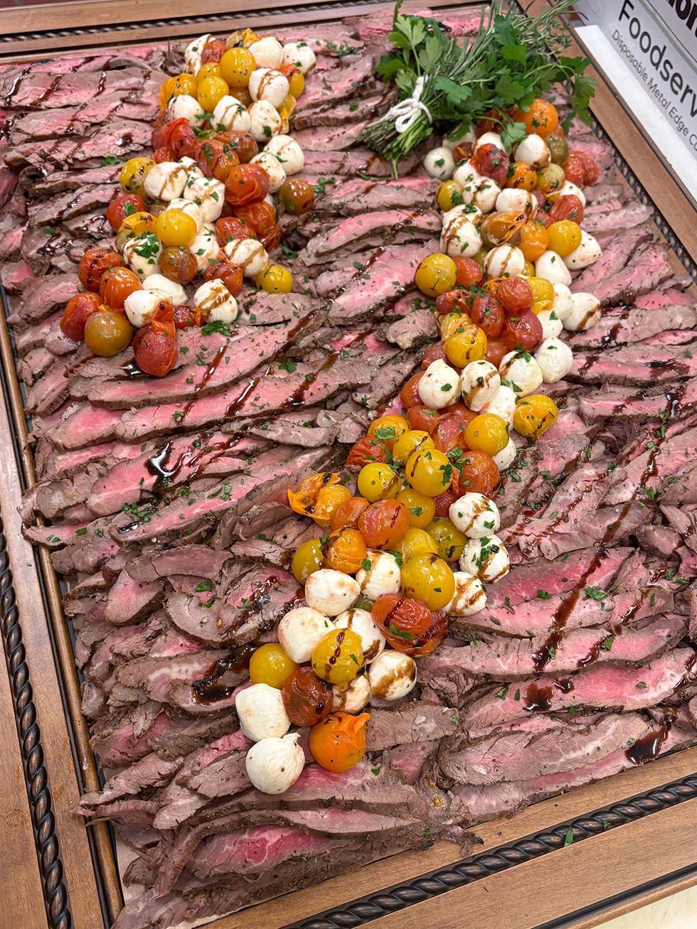 Thinly sliced roast beef platter topped with cherry tomatoes, herbs, and white onions