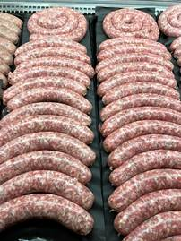 Rows of raw sausages on black trays in a refrigerated display case.