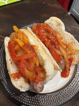 Two sausage sandwiches on a plate; topped with sauteed red and yellow peppers and onions.
