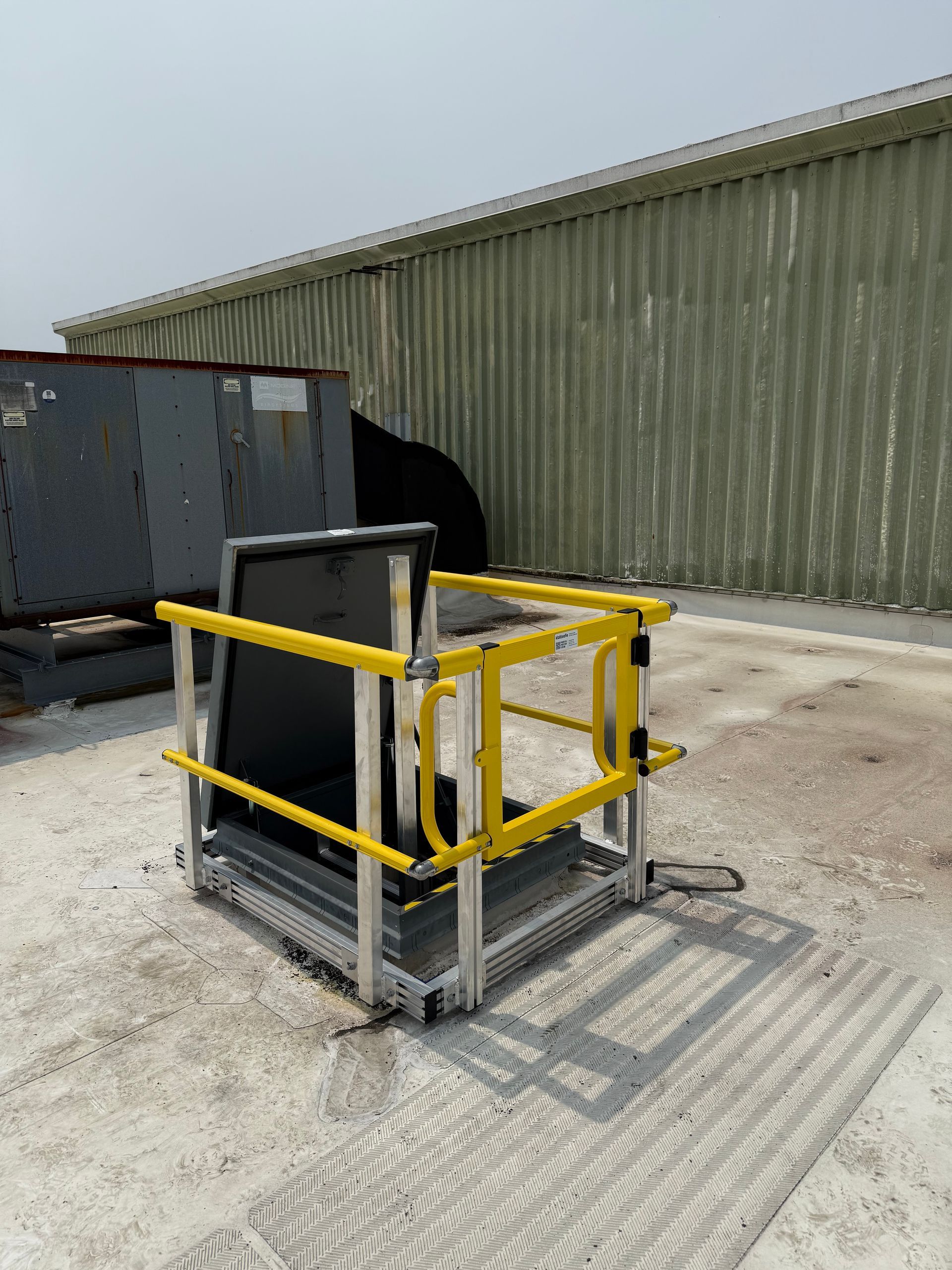A yellow safety railing system installed around an open roof hatch on a light-colored rooftop.