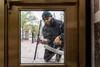 A person in a dark jacket and beanie seen through a glass door, holding a tool or piece of equipment.