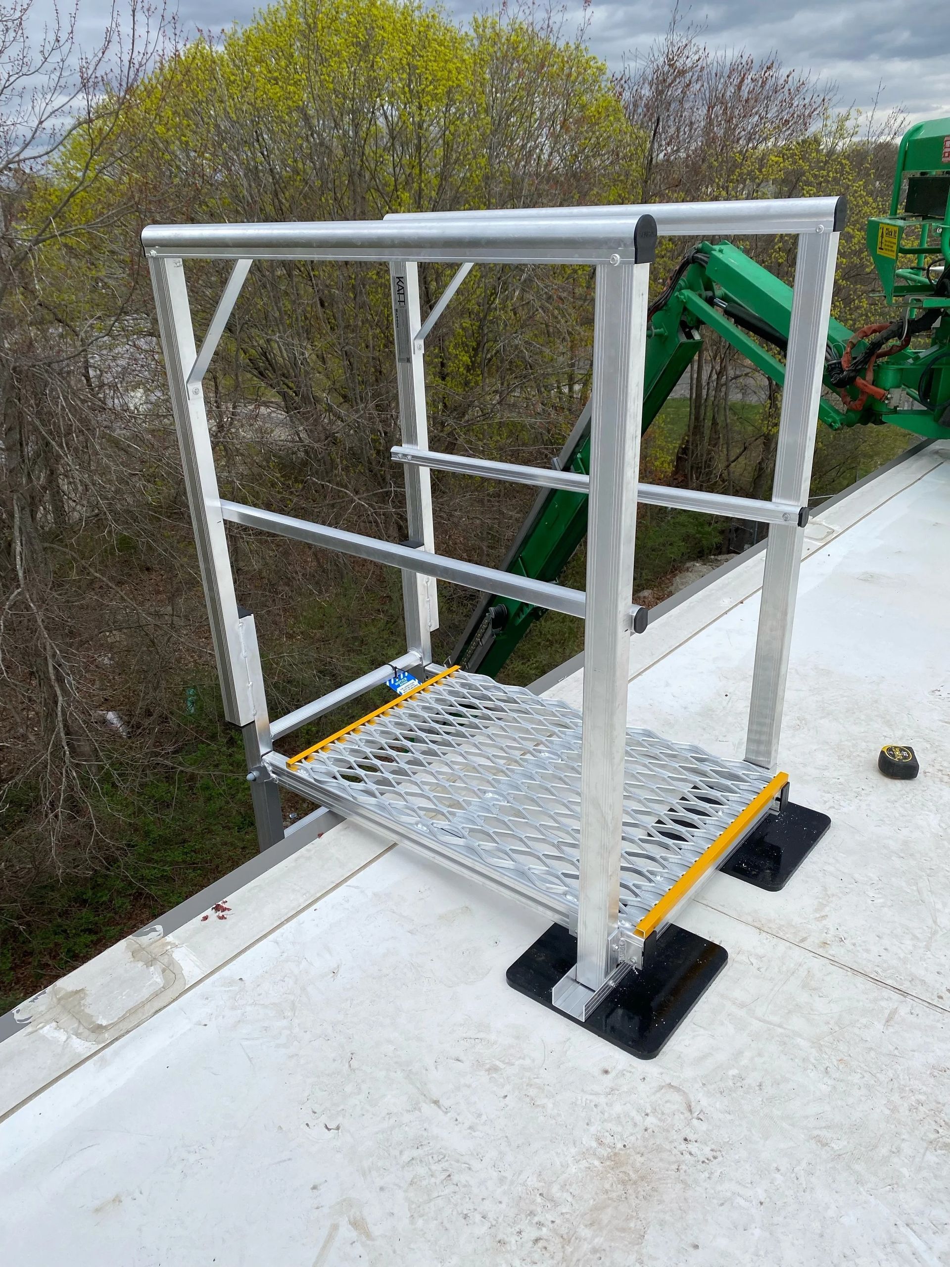 An aluminum safety crossover platform with a grated walkway and yellow-edged steps, installed on a white flat roof.