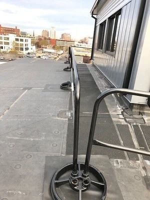 A black metal rooftop guardrail system stands on a flat, grey roof next to a building wall.