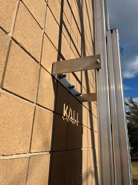 A metal bracket attached to a tan masonry wall, securing a vertical aluminum post.