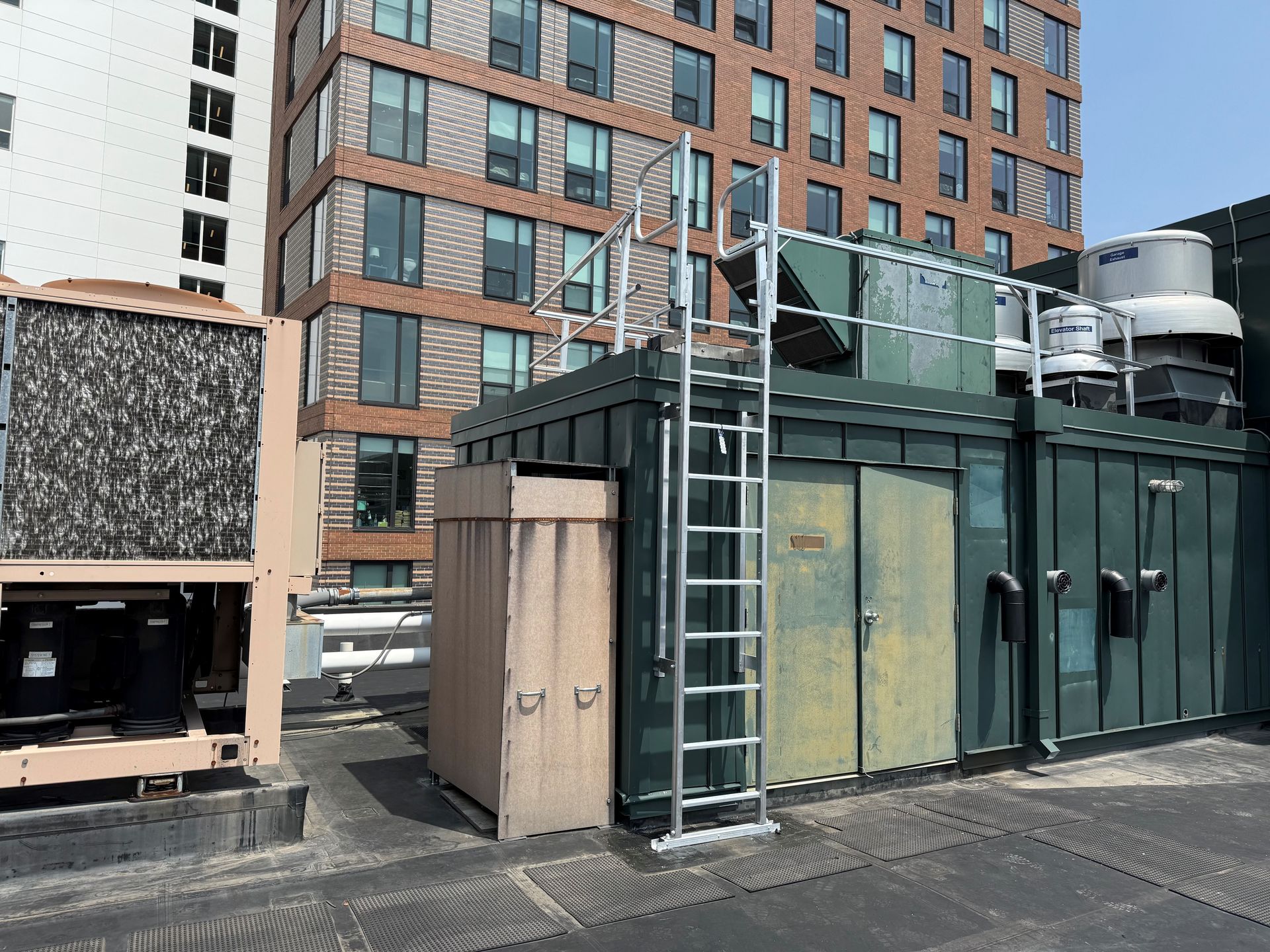 A rooftop mechanical area featuring a dark green equipment enclosure, a metal ladder, and a large air conditioning unit.