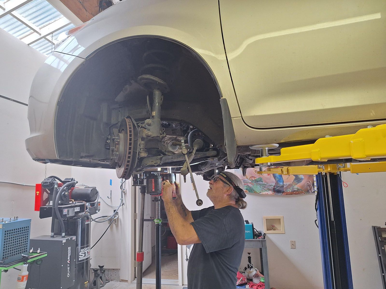 Mechanic working on a white car raised on a lift in a garage, using tools.
