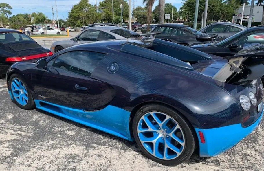 Blue and black Bugatti sports car parked, surrounded by other vehicles in a lot.
