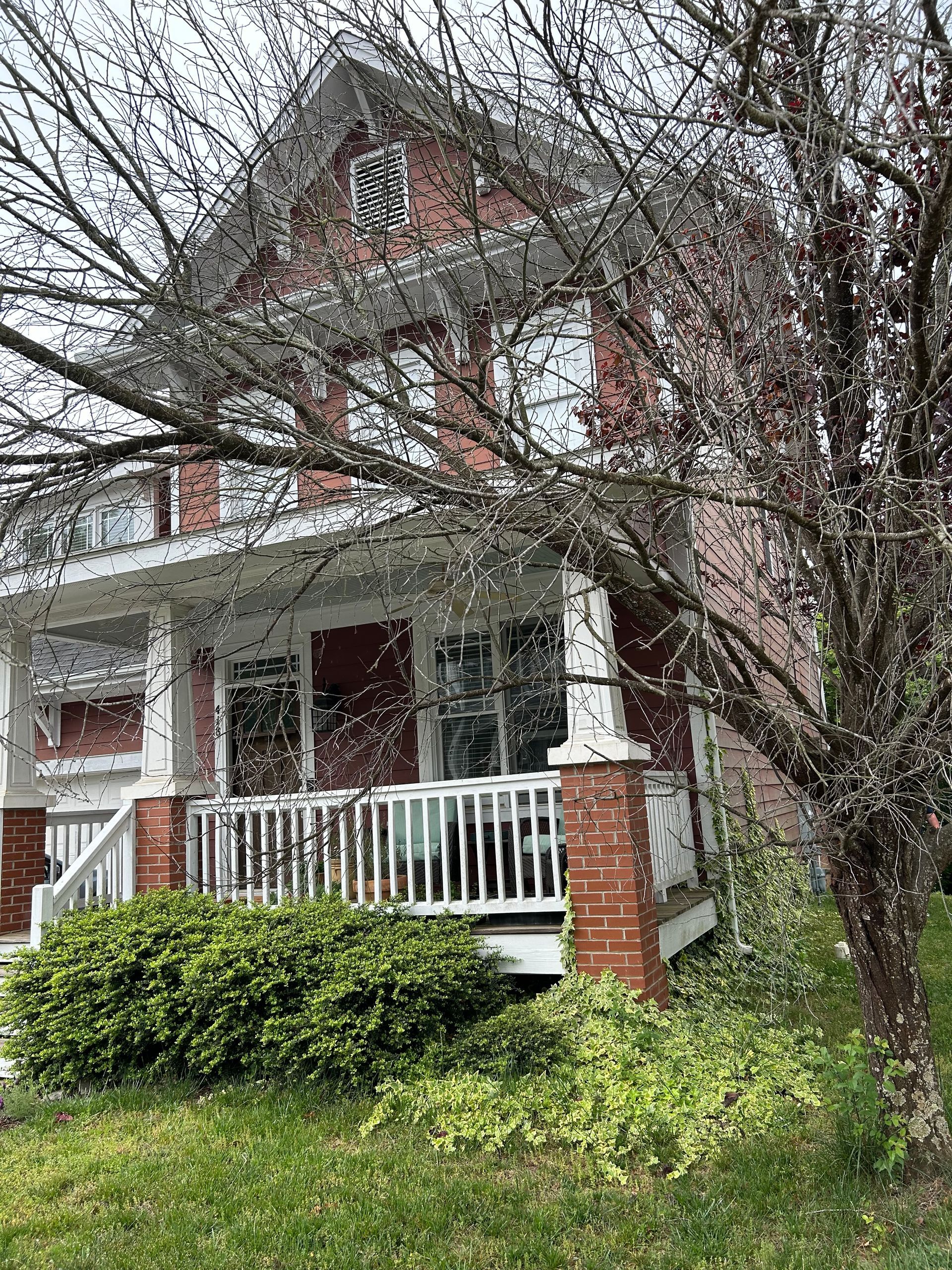A brick house with a porch and a white railing is surrounded by trees