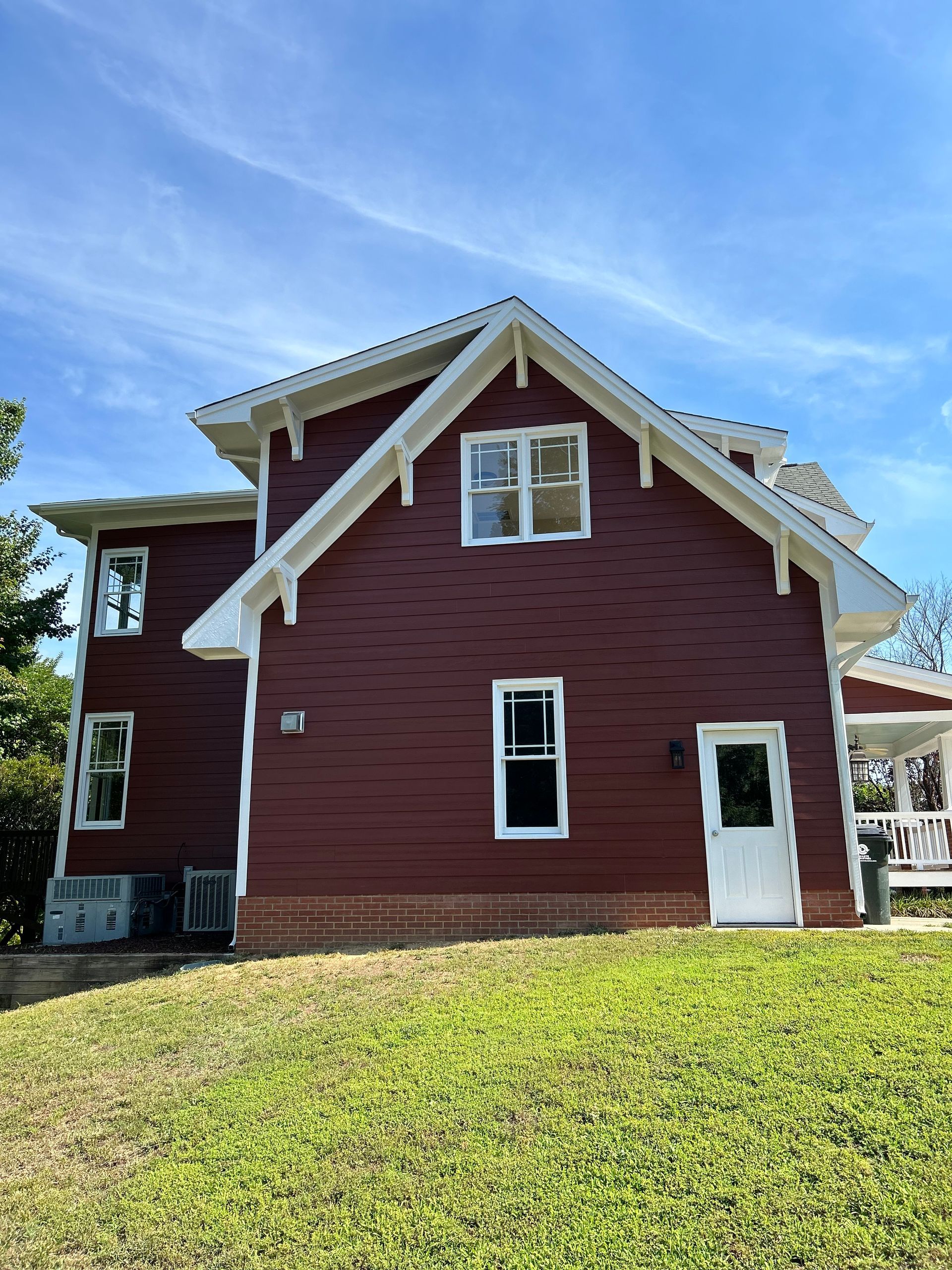 A red house with white trim is sitting on top of a grassy hill