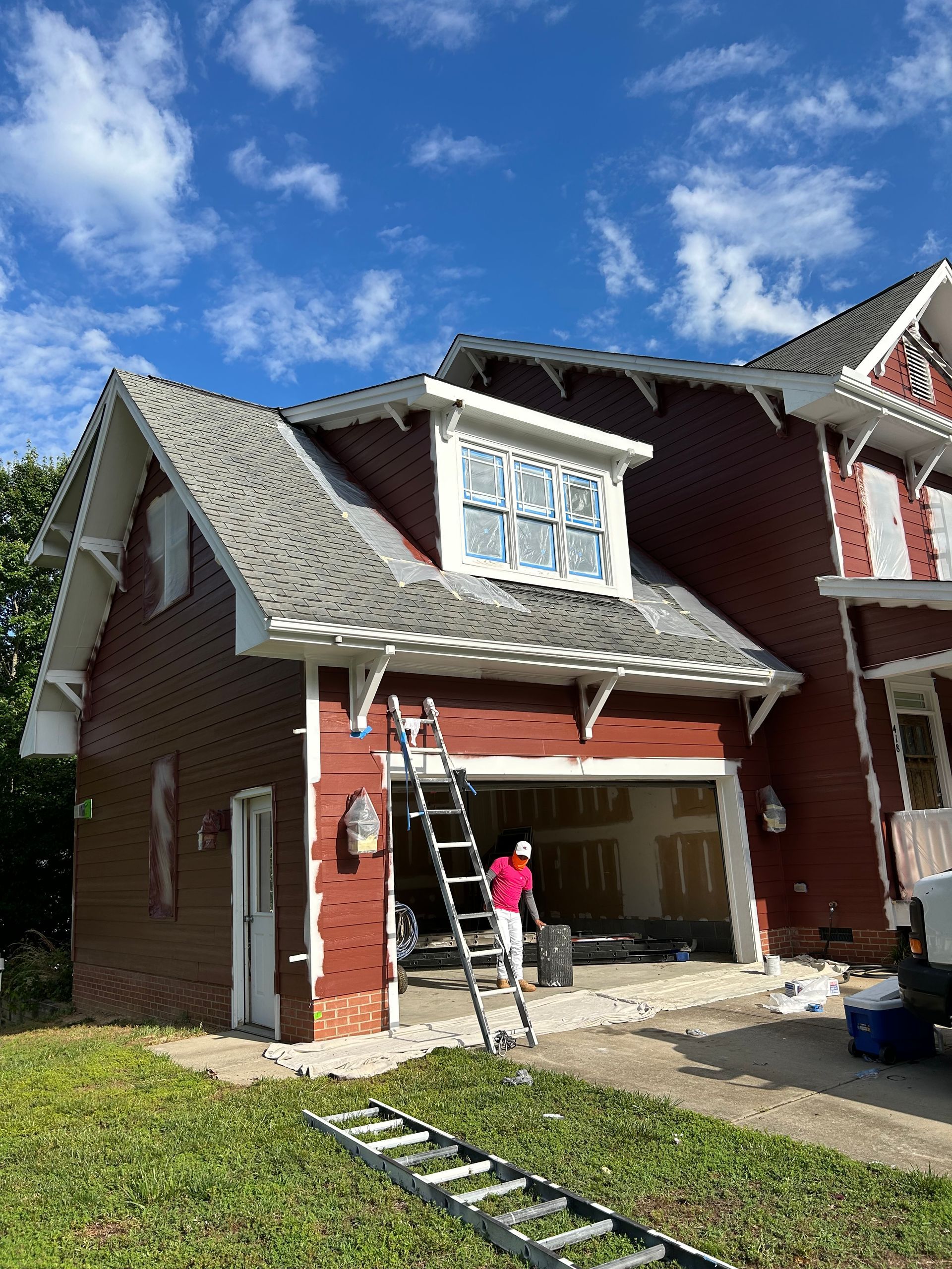A man is painting a red house with a ladder in front of it