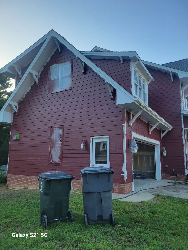 A man is painting a red house with a ladder in front of it