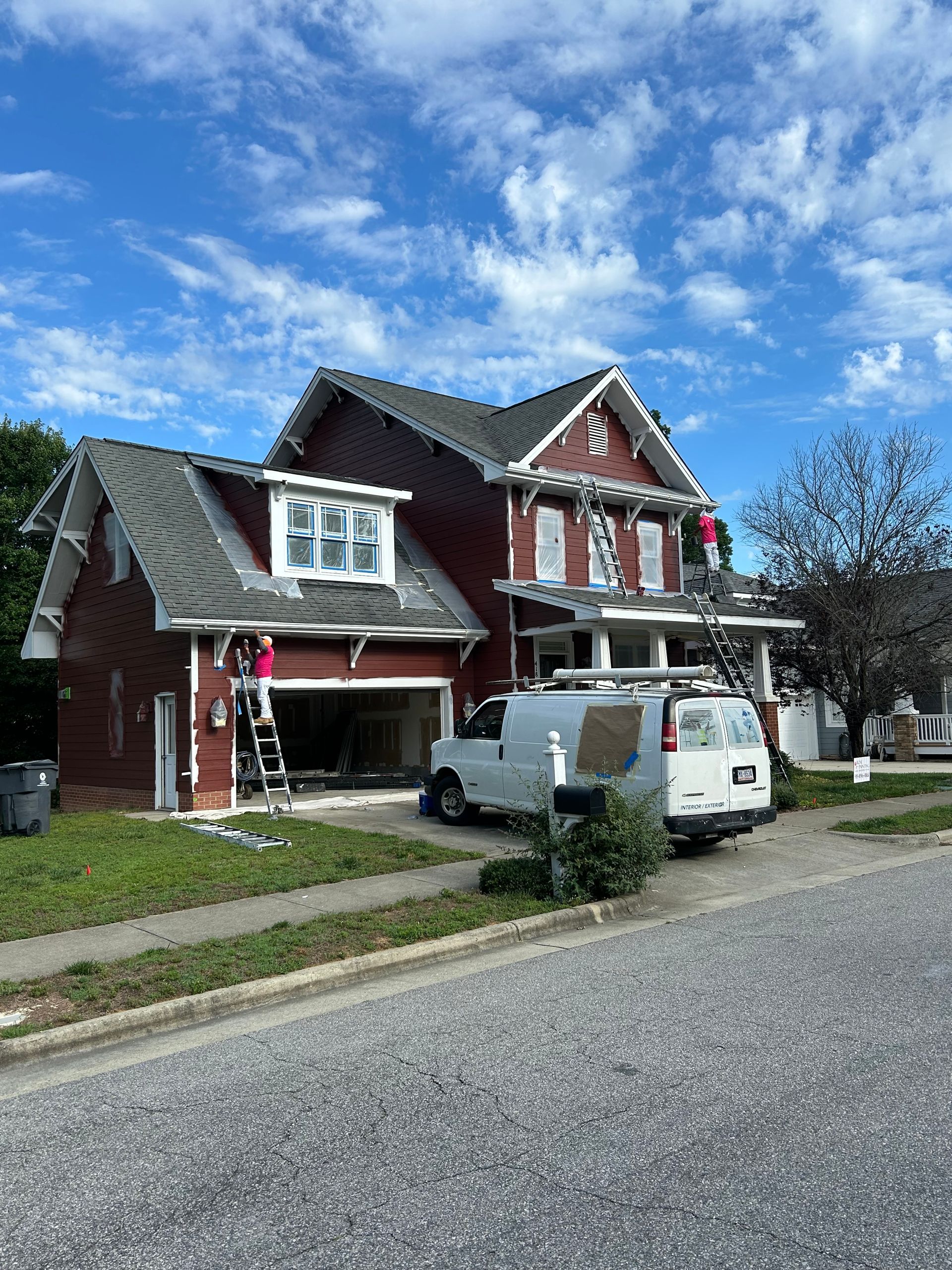A red house is being painted with a white van parked in front of it
