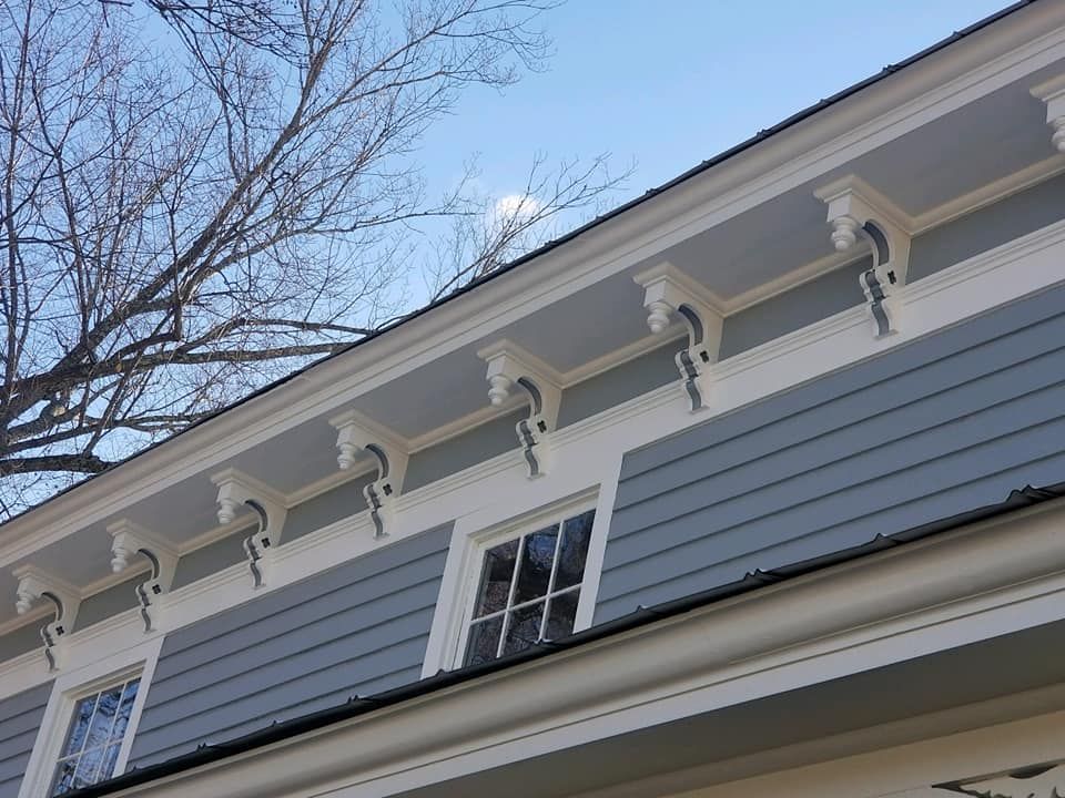 The roof of a house with a gray siding and white trim