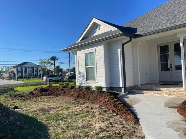 Single-story house with white siding, blue roof, and a curved front walkway by a freshly landscaped yard.