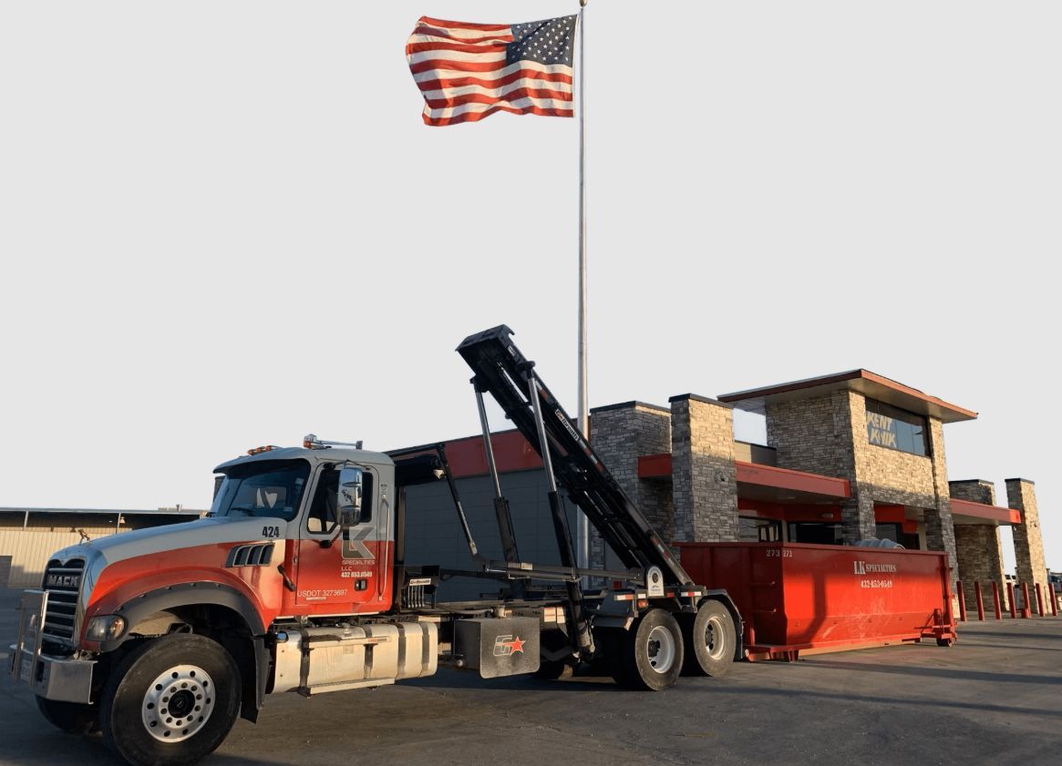 Red and gray waste disposal truck with red dumpster; American flag in the background.