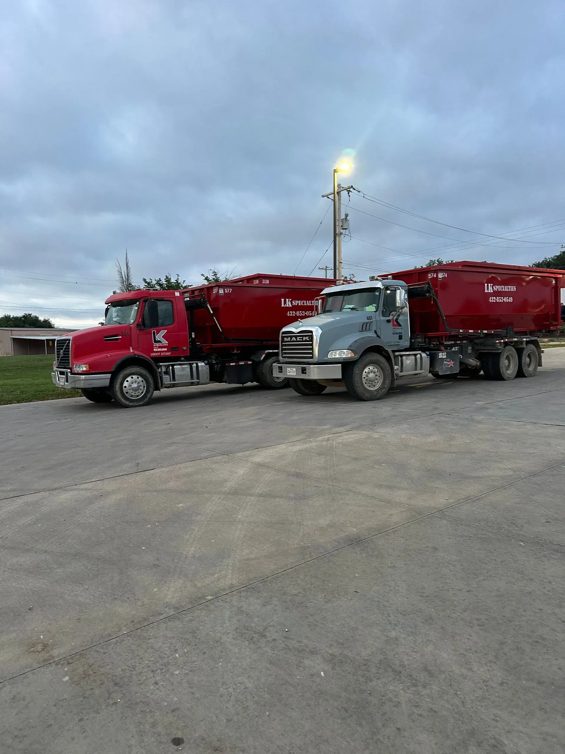 Two red and gray semi-trucks with tanker trailers parked on pavement.