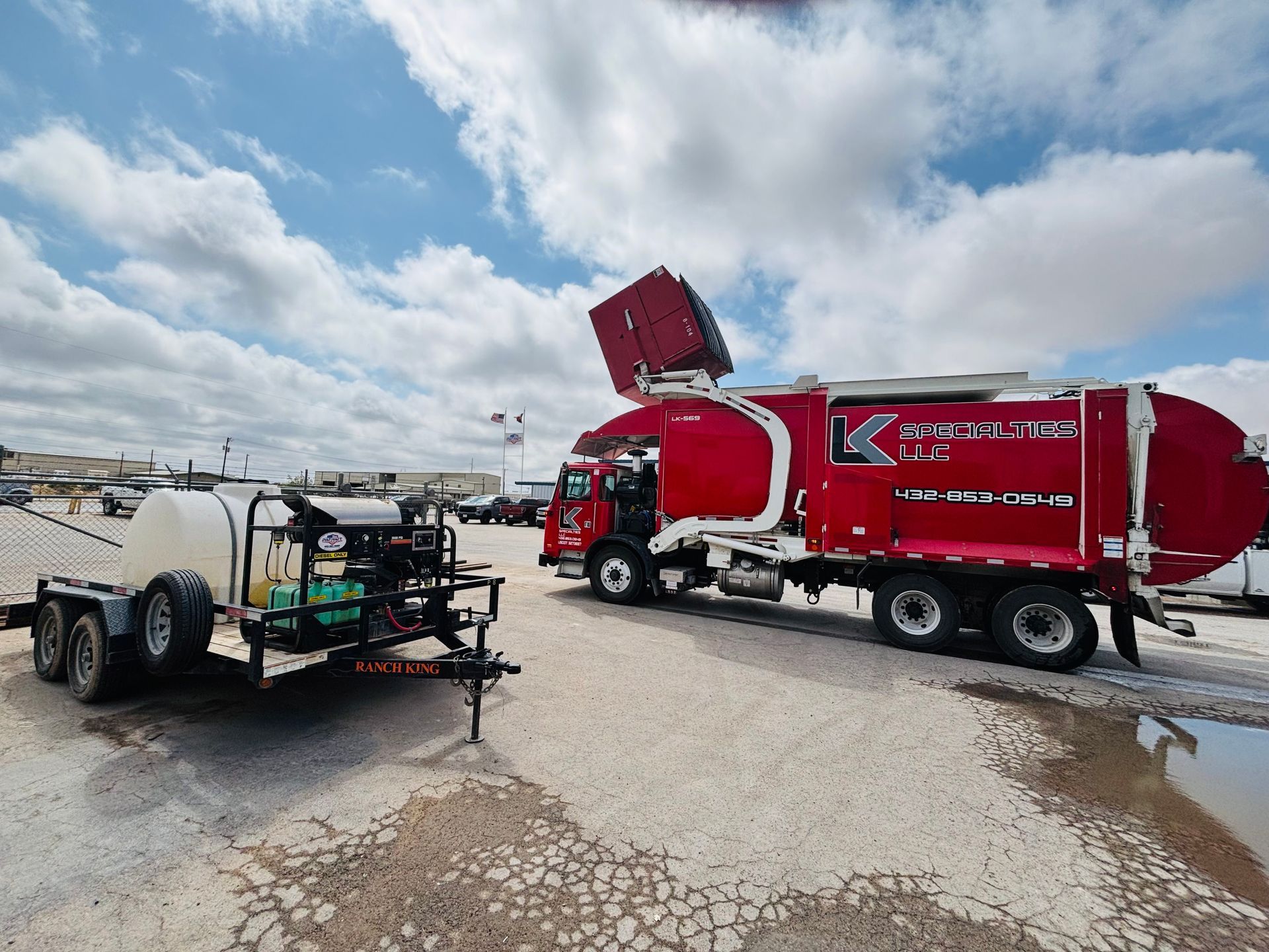A red sanitation truck and a white water trailer parked on gravel under a cloudy sky.