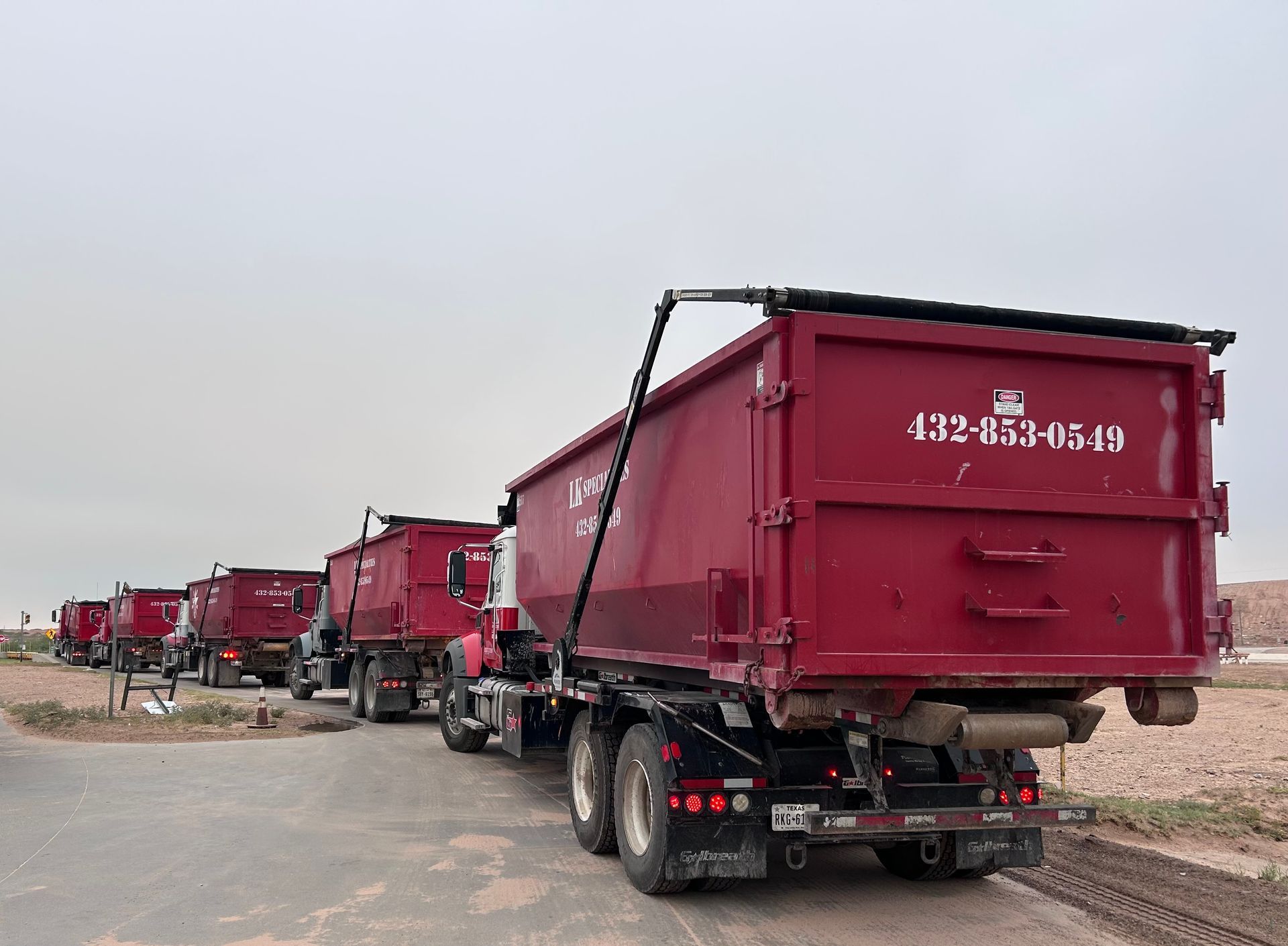 Red dump trucks lined up on a road, ready for hauling; overcast sky.