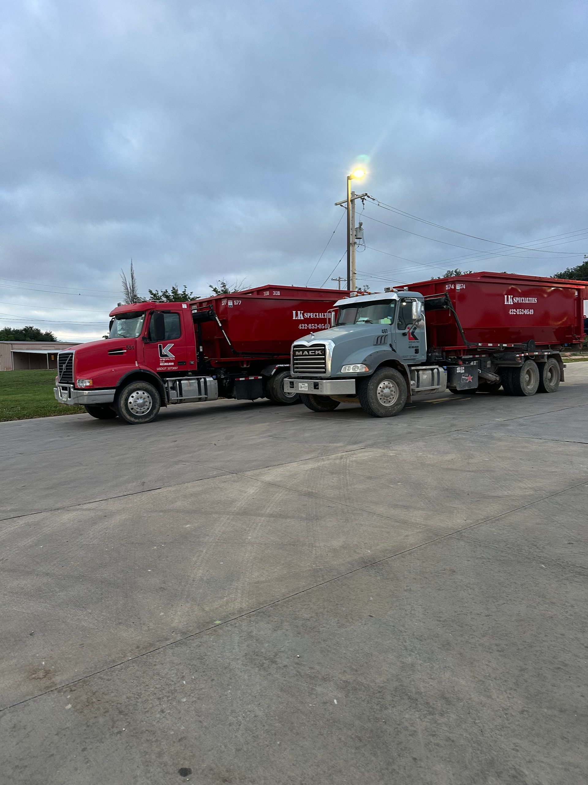 Two red and grey semi-trucks with tanker trailers parked on pavement under a cloudy sky.