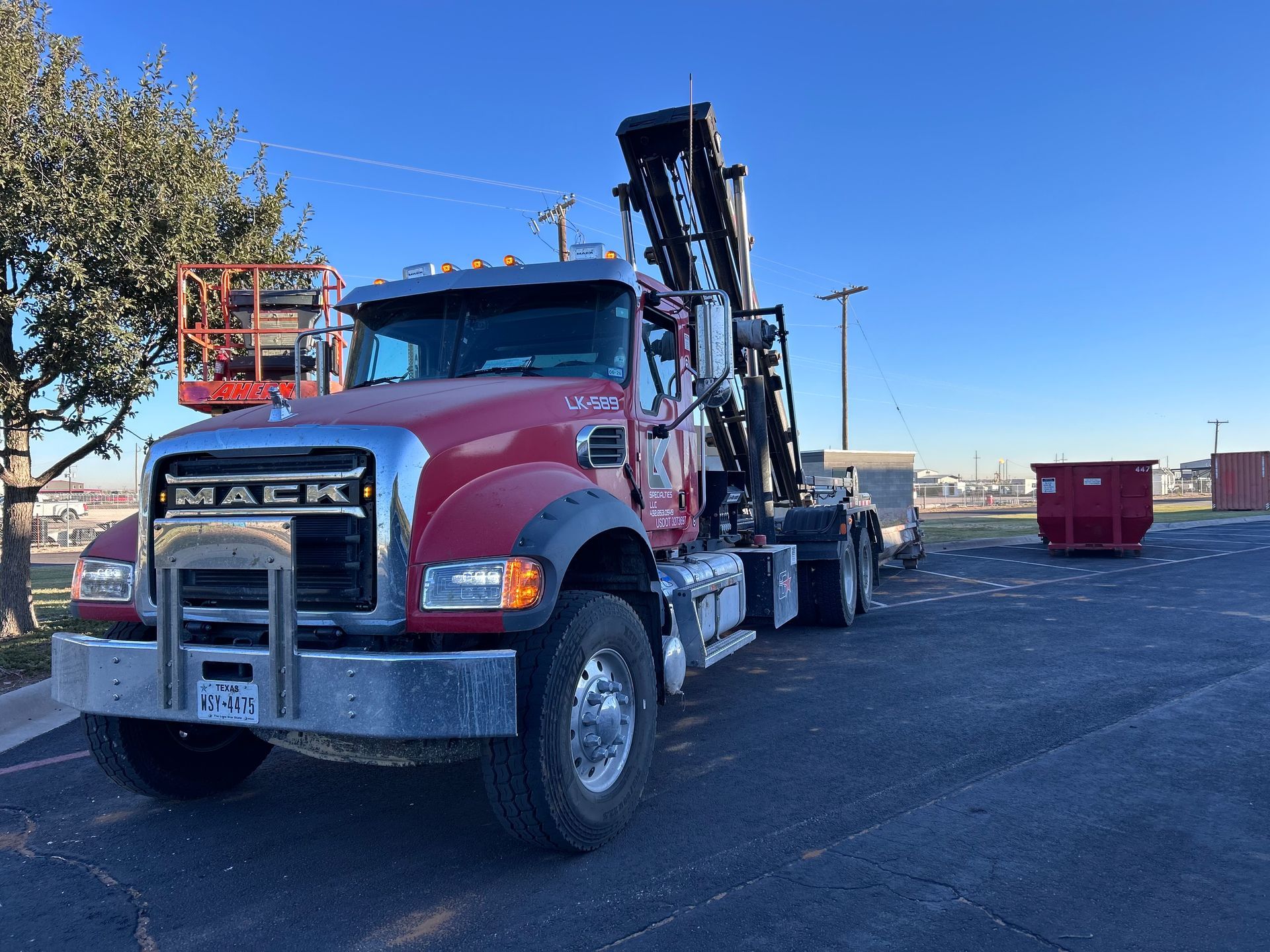 Red Mack truck with attached lift and dumpster in an asphalt parking lot.