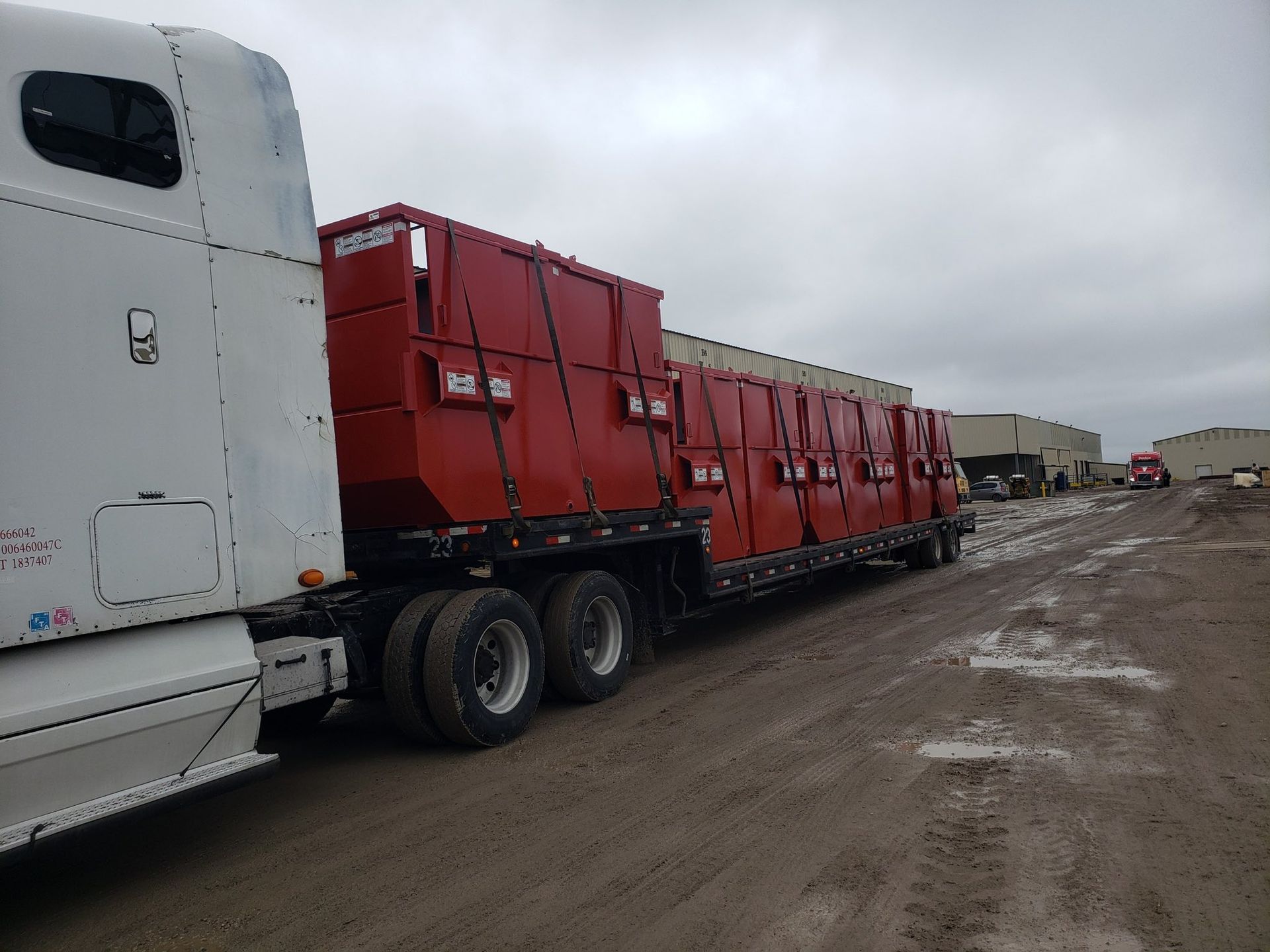 Red storage containers loaded on a semi-trailer truck parked on a muddy road.