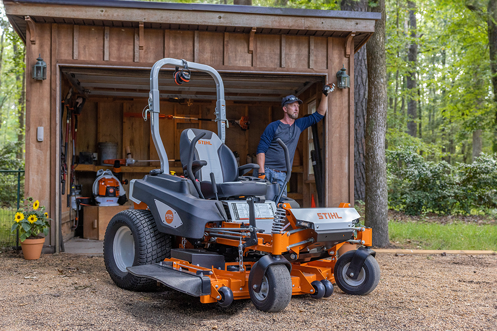 A man is standing next to a lawn mower in a garage.