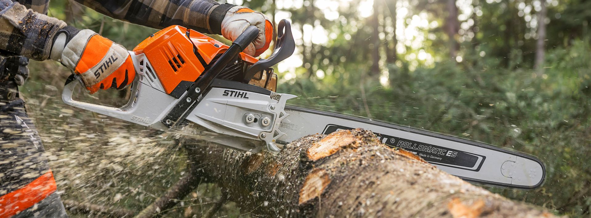 A man is using a chainsaw to cut a log in the woods.