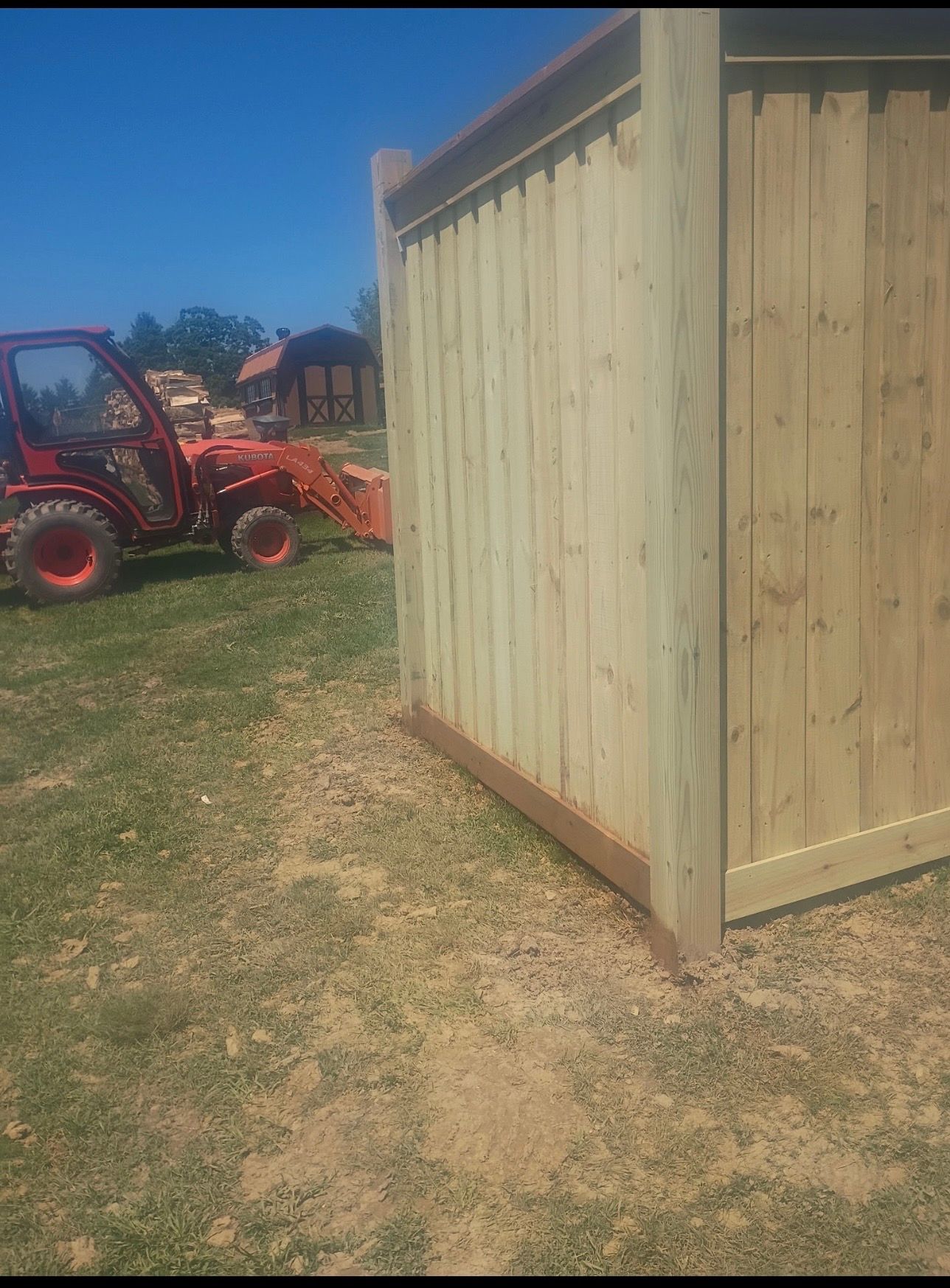 Wooden shed beside a red tractor on a grassy farm under a clear blue sky